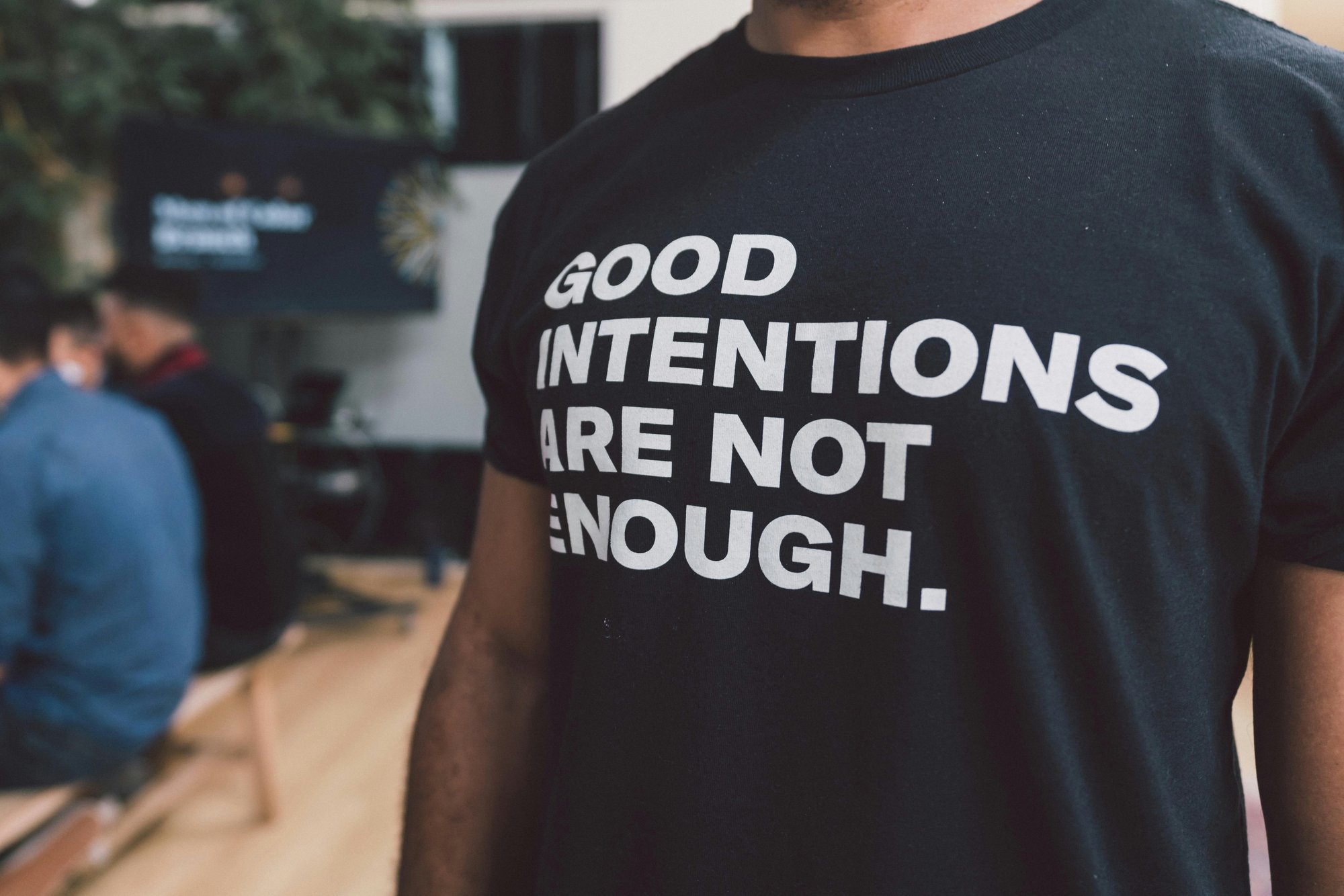 Man wearing a black t-shirt with white lettering that reads "Good intentions are not enough."